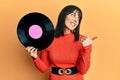 Young hispanic woman holding vinyl disc pointing thumb up to the side smiling happy with open mouth