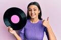 Young hispanic woman holding vinyl disc smiling happy and positive, thumb up doing excellent and approval sign Royalty Free Stock Photo