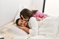 Young hispanic woman kissing her sleepy boyfriend at bed