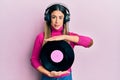 Young hispanic woman listening to music using headphones holding vinyl disc relaxed with serious expression on face