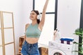 Young hispanic woman listening to music waiting for washing machine at laundry room Royalty Free Stock Photo