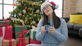 Young hispanic woman listening to music wearing headphones and christmas hat at home Royalty Free Stock Photo