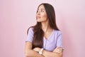 Young hispanic woman with long hair standing over pink background looking to the side with arms crossed convinced and confident Royalty Free Stock Photo