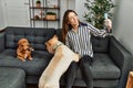 Young hispanic woman make selfie by the smartphone sitting on sofa with dogs at home