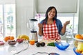 Young hispanic woman making healthy smoothie very happy and excited doing winner gesture with arms raised, smiling and screaming Royalty Free Stock Photo