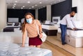 Young Hispanic woman in medical face mask looking for new mattress for bed in furniture store. Royalty Free Stock Photo