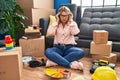 Young hispanic woman moving to a new home sitting on the floor with hand on head, headache because stress