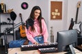 Young hispanic woman musician singing song playing piano keyboard at music studio Royalty Free Stock Photo