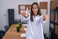 Young hispanic woman at the office approving doing positive gesture with hand, thumbs up smiling and happy for success Royalty Free Stock Photo