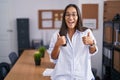 Young hispanic woman at the office success sign doing positive gesture with hand, thumbs up smiling and happy Royalty Free Stock Photo