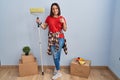 Young hispanic woman painting home walls with paint roller doing happy thumbs up gesture with hand Royalty Free Stock Photo