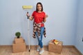 Young hispanic woman painting home walls with paint roller doing money gesture with hands, asking for salary payment, millionaire Royalty Free Stock Photo