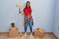 Young hispanic woman painting home walls with paint roller doing ok gesture shocked with surprised face, eye looking through Royalty Free Stock Photo