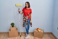 Young hispanic woman painting home walls with paint roller looking away to side with smile on face, natural expression Royalty Free Stock Photo