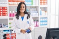 Young hispanic woman pharmacist using credit card and dataphone at pharmacy Royalty Free Stock Photo