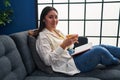 Young hispanic woman reading book and drinking coffee at home Royalty Free Stock Photo