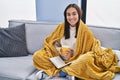 Young hispanic woman reading book and drinking coffee at home Royalty Free Stock Photo