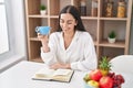 Young hispanic woman reading book drinking coffee at home Royalty Free Stock Photo