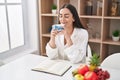 Young hispanic woman reading book drinking coffee at home Royalty Free Stock Photo
