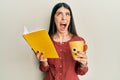 Young hispanic woman reading book drinking cup of tea angry and mad screaming frustrated and furious, shouting with anger looking Royalty Free Stock Photo