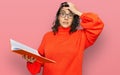 Young hispanic woman reading a book wearing glasses stressed and frustrated with hand on head, surprised and angry face Royalty Free Stock Photo