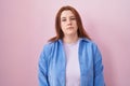 Young hispanic woman with red hair standing over pink background looking sleepy and tired, exhausted for fatigue and hangover, Royalty Free Stock Photo
