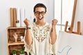 Young hispanic woman with short hair at art studio excited for success with arms raised and eyes closed celebrating victory Royalty Free Stock Photo