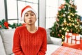 Young hispanic woman with short hair wearing christmas hat sitting on the sofa looking at the camera blowing a kiss on air being Royalty Free Stock Photo