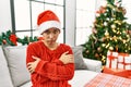 Young hispanic woman with short hair wearing christmas hat sitting on the sofa shaking and freezing for winter cold with sad and Royalty Free Stock Photo