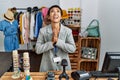 Young hispanic woman with short hair working as manager at retail boutique begging and praying with hands together with hope