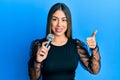Young hispanic woman singing song using microphone smiling happy and positive, thumb up doing excellent and approval sign Royalty Free Stock Photo