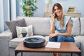 Young hispanic woman sitting at home by vacuum robot speaking on the phone looking positive and happy standing and smiling with a Royalty Free Stock Photo