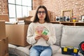 Young hispanic woman sitting on the sofa at new home holding money puffing cheeks with funny face Royalty Free Stock Photo