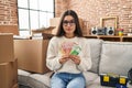 Young hispanic woman sitting on the sofa at new home holding money relaxed with serious expression on face Royalty Free Stock Photo