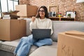 Young hispanic woman sitting on the sofa at new home using laptop looking at the camera smiling with open arms for hug Royalty Free Stock Photo