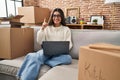 Young hispanic woman sitting on the sofa at new home using laptop pointing thumb up to the side smiling happy with open mouth Royalty Free Stock Photo