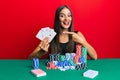 Young hispanic woman sitting on the table playing poker holding cards smiling happy pointing with hand and finger Royalty Free Stock Photo