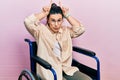 Young hispanic woman sitting on wheelchair doing funny gesture with finger over head as bull horns