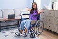 Young hispanic woman sitting on wheelchair at home looking at the camera smiling with open arms for hug Royalty Free Stock Photo