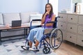 Young hispanic woman sitting on wheelchair at home looking confident at the camera smiling with crossed arms and hand raised on Royalty Free Stock Photo