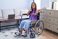 Young hispanic woman sitting on wheelchair at home smiling and looking at the camera pointing with two hands and fingers to the Royalty Free Stock Photo