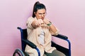 Young hispanic woman sitting on wheelchair punching fist to fight, aggressive and angry attack, threat and violence