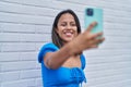 Young hispanic woman smiling confident making selfie by the smartphone over white isolated brick background Royalty Free Stock Photo