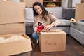 Young hispanic woman smiling confident packing fragile package at new home