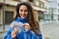 Young hispanic woman smiling happy counting sweden krone banknotes at the city