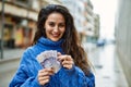 Young hispanic woman smiling happy counting sweden krone banknotes at the city