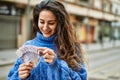 Young hispanic woman smiling happy counting sweden krone banknotes at the city