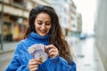 Young hispanic woman smiling happy counting sweden krone banknotes at the city