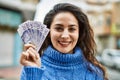 Young hispanic woman smiling happy holding sweden krone banknotes at the city
