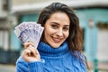 Young hispanic woman smiling happy holding sweden krone banknotes at the city